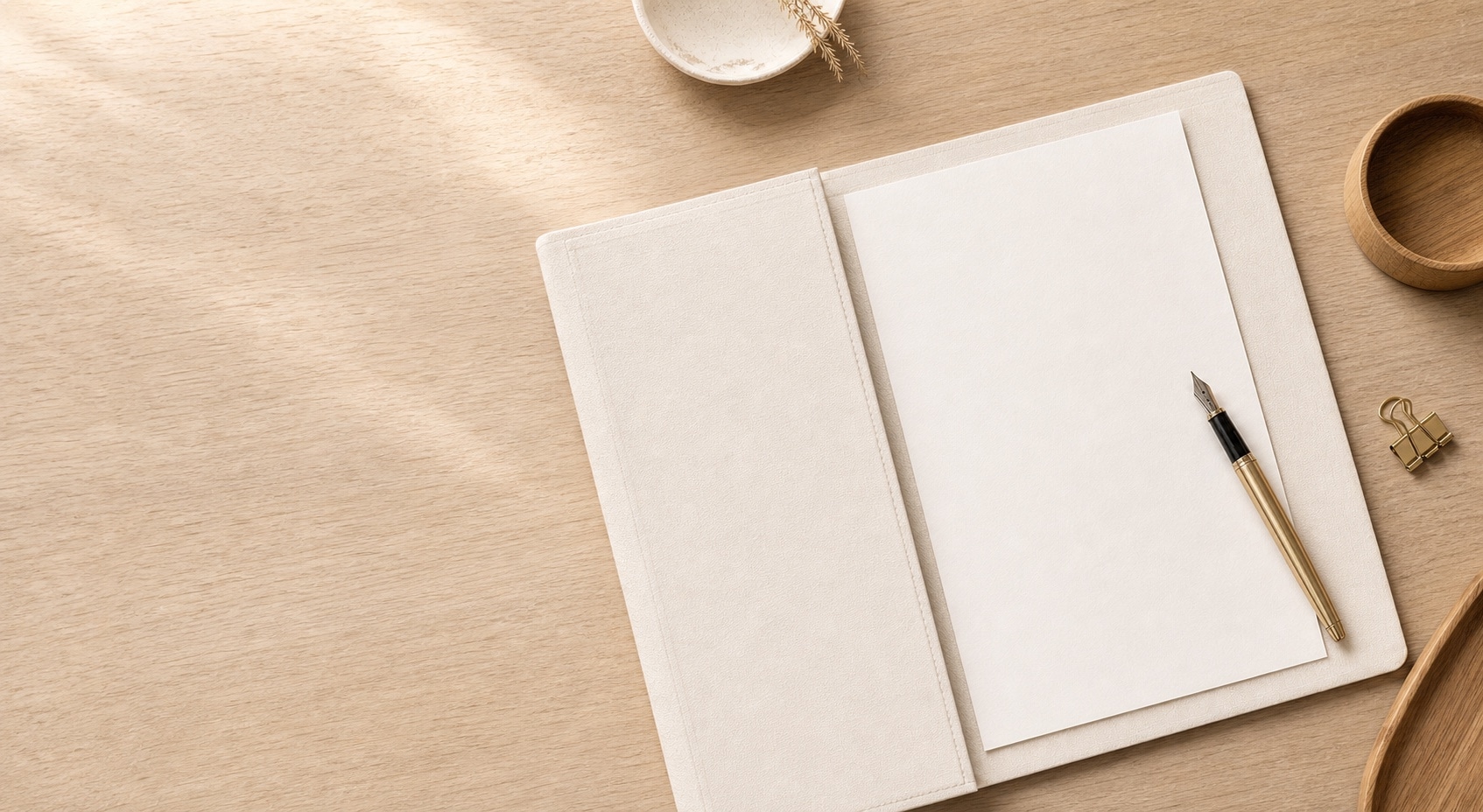 An open cream notebook and fountain pen on a warm timber desk
